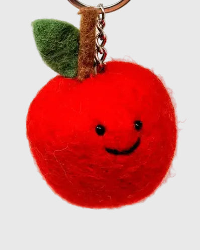 A red felt apple keychain with a smiling face, a green felt leaf, a brown felt stem, and a metal key ring on a white background.