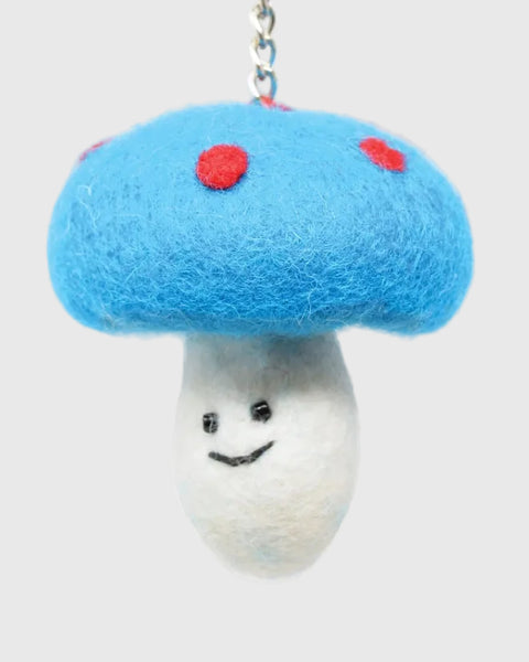 A cute felt mushroom keychain charm with a bright blue felt cap, red felt spots, a white felt stem, and a smiling face. It features a silver metal key ring at the top and is photographed on a clean white background.