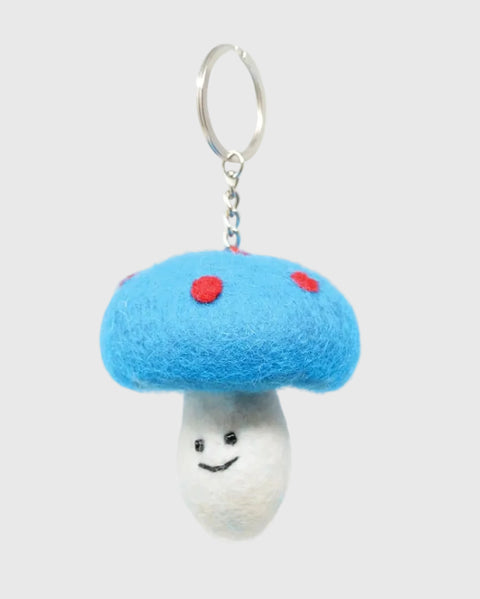 A felt mushroom keychain charm with a bright blue cap, red spots, and a white smiling stem, attached to a silver metal key ring on a plain white background.