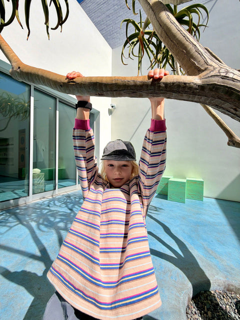 Child in a colorful striped dress holding onto a large branch with a modern building in the background
